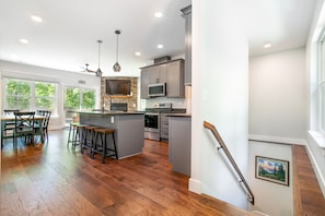Une cuisine spacieuse dotée d’un îlot central, un coin repas avec une table et des chaises en bois, et un escalier avec une rampe.