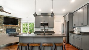 Una cocina moderna con una isla central, gabinetes grises y un televisor grande montado en una pared de piedra.