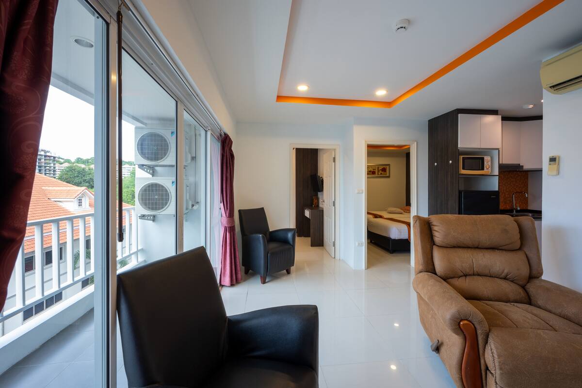 Una habitación de hotel moderna con balcón, sofá, sillón y cama.