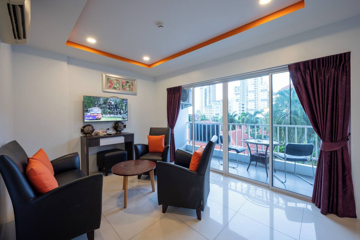 Una sala de estar moderna con un televisor de pantalla plana, asientos cómodos y un balcón con mobiliario exterior.
