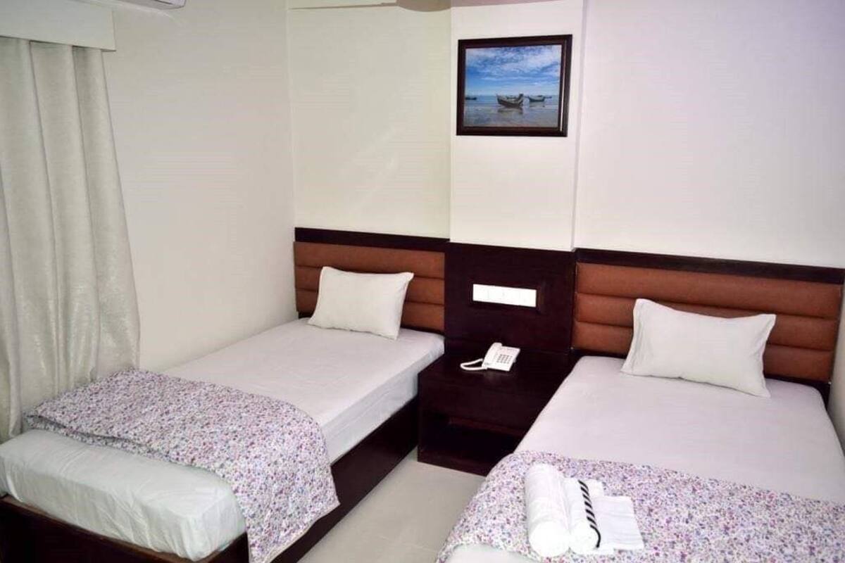 A hotel room with two single beds, a bedside table with a phone, and a picture on the wall.