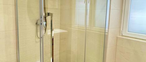 A modern bathroom with a glass-enclosed shower, a toilet, and a sink.