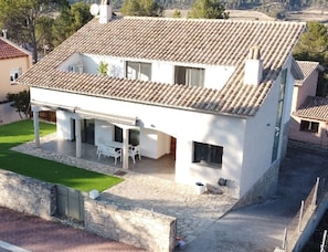 A two-story house with a tiled roof, a covered patio with outdoor furniture, and a stone wall surrounding the property. - Chalet a 35 Minutos de Barcelona, con Todos los Alicientes Para Disfrutar (Els Pinyerets)