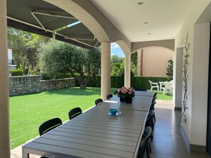 Une terrasse extérieure avec une longue table et des chaises, entourée d’un mur de pierre et de verdure.
