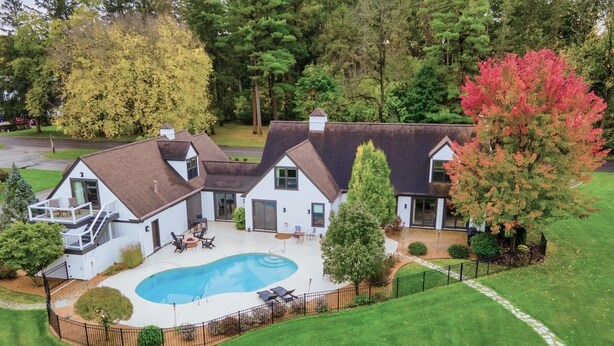 Ein zweistöckiges Haus mit Swimmingpool, überdachter Terrasse und umzäunter Garten.