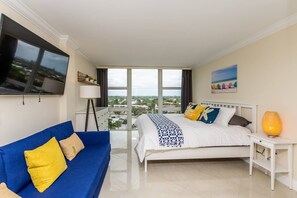 A hotel room with a bed, a blue sofa, a TV, a lamp, and a city view.