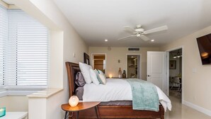 Quarto com cama, mesa de cabeceira, abajur e ventilador de teto.