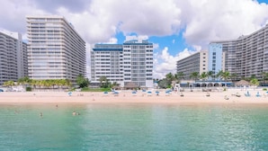 Et strandhotel med flere høje bygninger, en sandstrand og parasoller.