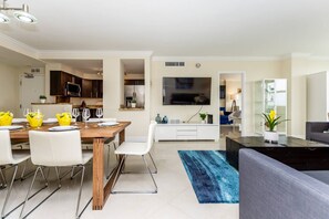 A modern living space with a dining area, kitchen, and a seating area with a flat-screen TV.