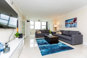 A modern living room with a flat-screen TV, two grey sofas, a coffee table, and a blue rug.