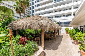A hotel courtyard with a thatched-roof structure, outdoor seating, and lush greenery.