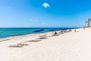 A beach with sun loungers and umbrellas, a clear sky, and the ocean.