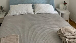 A neatly made bed with a quilted grey bedspread, two white pillows, and a framed abstract map on the wall. - Two-room apartment for 4 people with garden and patio located in the heart of Porto Pollo.  (Porto Pollo)