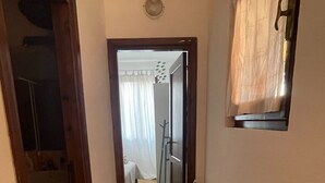 A narrow hallway with a wooden door, a white wall, and a window with a curtain. - Two-room apartment for 4 people with garden and patio located in the heart of Porto Pollo.  (Porto Pollo)