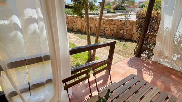 A covered outdoor seating area with a wooden bench and a table with a vase of flowers. - Two-room apartment for 4 people with garden and patio located in the heart of Porto Pollo.  (Porto Pollo)