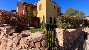 A two-story building with a yellow facade and a stone wall in the foreground. - Two-room apartment for 4 people with garden and patio located in the heart of Porto Pollo.  (Porto Pollo)