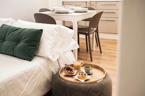 A neatly made bed with a green pillow, a breakfast tray with pastries and a glass of orange juice, and a dining area with a table set for two. - Domina Apartments Rome - Saint Peter 2 (Roma)