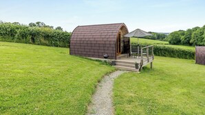A small, curved-roofed structure with a wooden deck and outdoor seating, surrounded by a grassy field and a hedge. - 1 bedroom accommodation in Ross-on-Wye (Ross-on-Wye)
