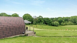 A modern building with a dark roof, a covered outdoor seating area, and a grassy field with trees in the background. - 1 bedroom accommodation in Ross-on-Wye (Ross-on-Wye)