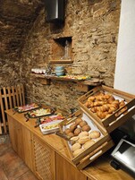 Buffet com diversos alimentos, incluindo saladas, carnes e doces, em sala com paredes de pedra rústica.