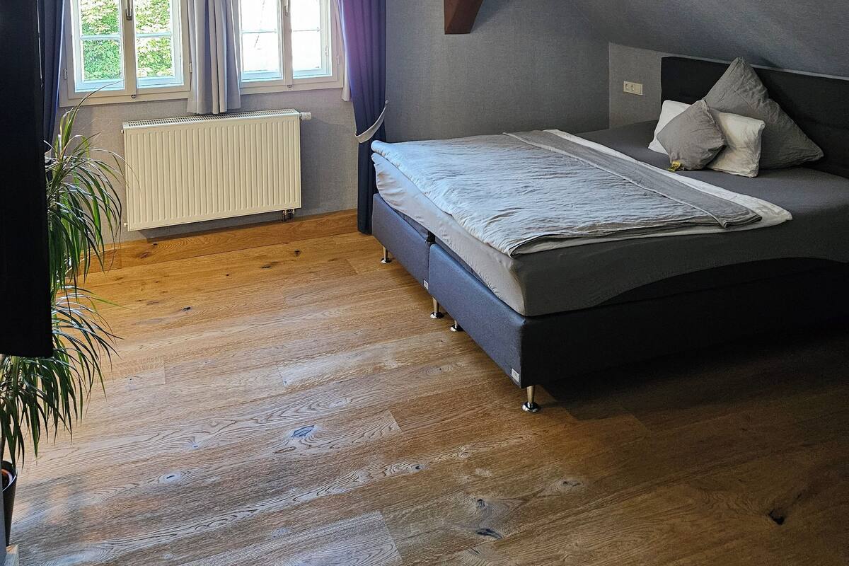 A bedroom with a bed, a radiator, a window with curtains, and a plant.