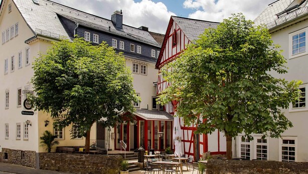 A traditional European building with a restaurant sign, a stone wall, and outdoor seating. - Hotel zum Löwen Herborn (Herborn)