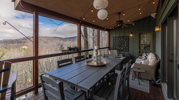 A covered outdoor dining area with a table and chairs, string lights, and a view of the surrounding landscape. - The Raven (Banner Elk)