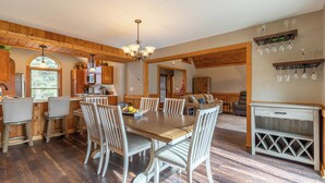 A spacious kitchen with wooden beams, a dining area with a large table and chairs, and a living area with a sofa and TV. - White Tail Cottage (Banner Elk)