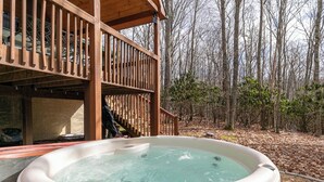 A hot tub in a wooden deck area with a forest backdrop. - White Tail Cottage (Banner Elk)