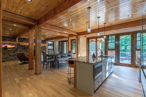 A spacious kitchen with a large island, wooden beams, and a stone accent wall. - Whiskey River Lodge at Eagles Nest (Banner Elk)