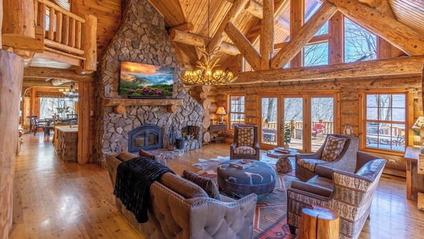Un intérieur spacieux de chalet en bois, avec une cheminée en pierre, des poutres apparentes et de grandes fenêtres.