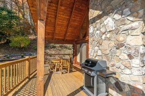A covered outdoor area with a stone wall, a wooden deck, and a barbecue grill. - Ambleside (Vilas)