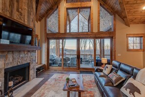 A spacious living room with a stone fireplace, leather sofa, and large sliding glass doors leading to an outdoor deck. - Happy Trails at Eagles Nest (Elk Park)