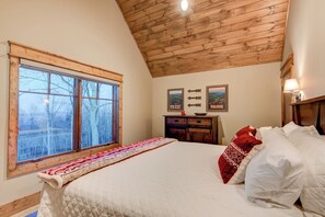 A bedroom with a large bed, a wooden ceiling, a window with a view of trees, a dresser, and two wall-mounted signs. - Happy Trails at Eagles Nest (Elk Park)