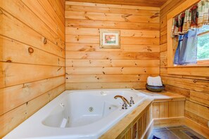 Une cabane en bois avec une grande baignoire, un tableau encadré au mur et une fenêtre avec des rideaux.