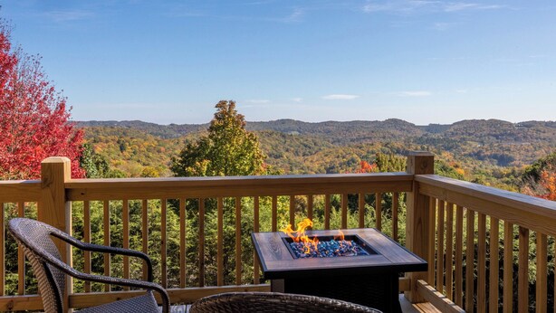 A wooden deck with a fire pit and a chair, overlooking a forested mountain range. - Blue Ridge Blessing (Blowing Rock)