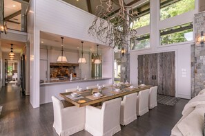 A spacious dining area with a long table, white chairs, and pendant lighting. - The Outside Inn at Eagles Nest (Banner Elk)