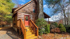 A wooden cabin with a red door, stone chimney, and a wooden staircase leading to the entrance. - Moonlight Lodge (Fleetwood)