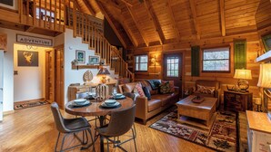 A cozy log cabin interior with a dining area, a sofa, and a staircase leading to an upper level. - Moonlight Lodge (Fleetwood)