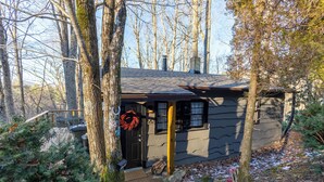 A small cabin with a dark door, a wreath hanging on the door, and a wooden deck. - Boone Folly (Boone)