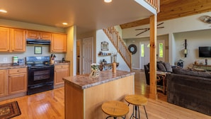 A spacious kitchen with wooden cabinets, a black stove, and a wooden island with stools. - 4 Bears Lodge (Banner Elk)