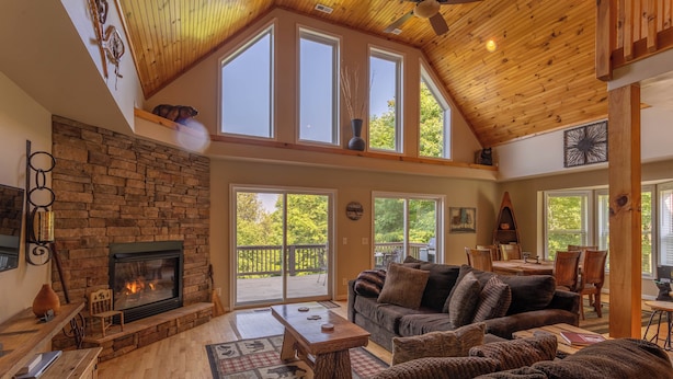 A spacious living room with a stone fireplace, wooden ceiling, and large windows. - 4 Bears Lodge (Banner Elk)
