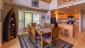 A spacious dining area with a wooden table and chairs, a kitchen with wooden cabinets, and a view of the outdoors through large windows. - 4 Bears Lodge (Banner Elk)