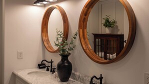 A bathroom with two large wooden-framed mirrors, a marble sink, and a black vase with green plants. - Gone Ski'Inn (Banner Elk)