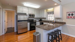 A modern kitchen with white cabinets, stainless steel appliances, a granite countertop, and a bar stool area. - Gone Ski'Inn (Banner Elk)