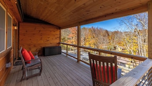 A wooden deck with a bench and a chair, overlooking a forest with autumn foliage. - Whiskey Rock (Banner Elk)