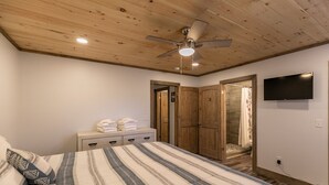 A bedroom with a bed, a wooden ceiling, a ceiling fan, a TV, and a bathroom door. - Whiskey Rock (Banner Elk)