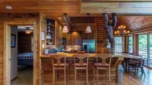 Ein Interieur einer Holzhütte mit Küche, Essbereich und einer Bärenskulptur.