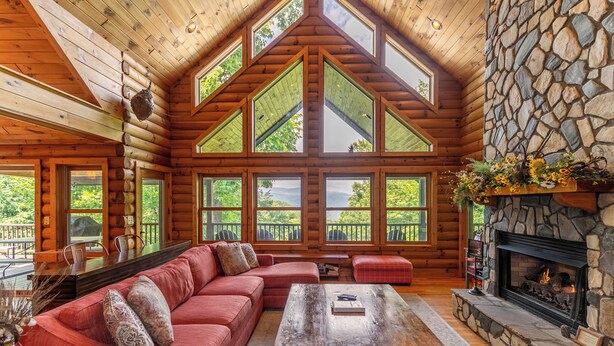 Ein Holzhütten-Interieur mit einer großen Holzbalkendecke, einem Kamin aus Stein und einem roten, modularen Sofa.