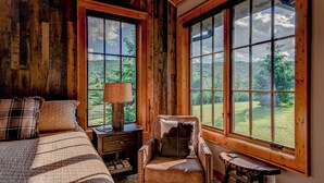 A rustic room with a large window, a bed, a chair, and a nightstand. - Banner View (Banner Elk)